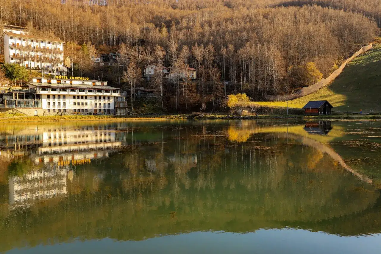Hotel Cristallo al Passo del Cerreto, con riflessi sull'acqua calma e un bosco autunnale sullo sfondo.