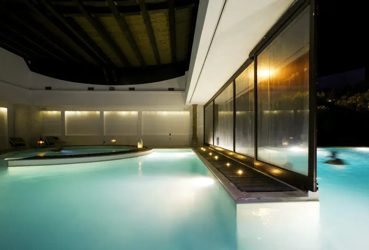 Piscina interna illuminata, con vasca idromassaggio e vista sulle terme Viterbo Salus. Relax e benessere notturno.