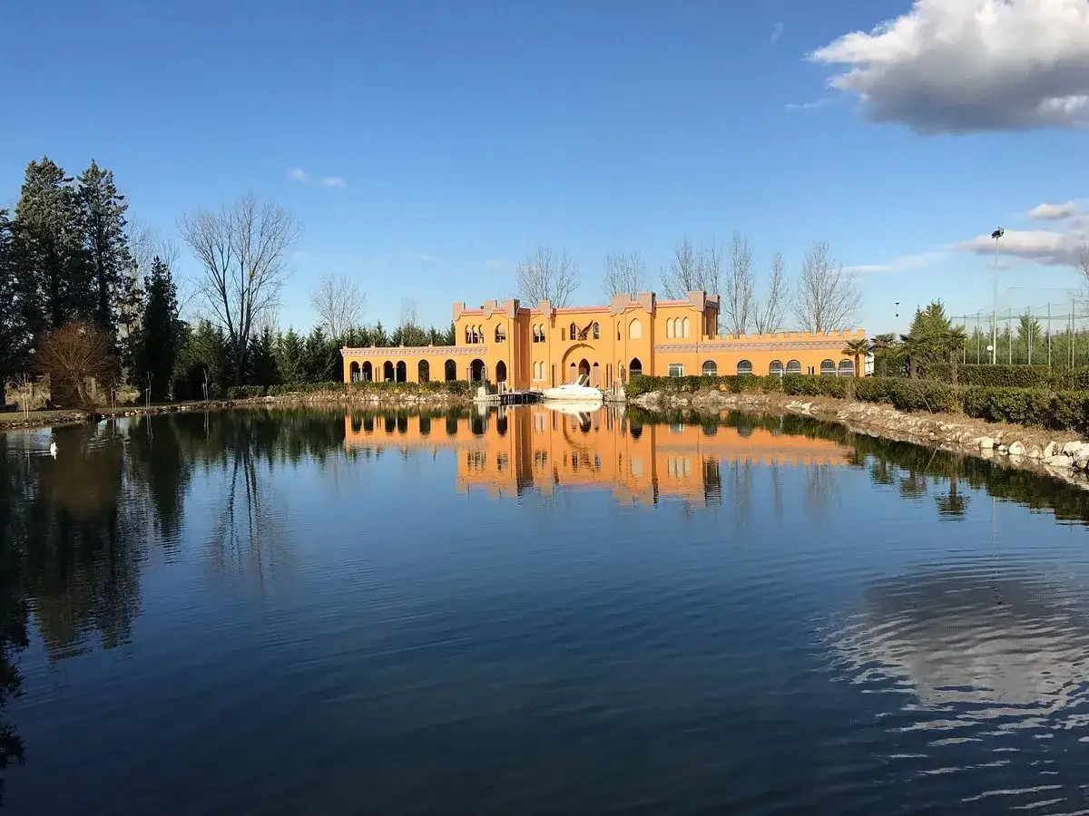 Edificio arancione con portico ad archi si specchia in un lago tranquillo, un'oasi di pace che ricorda le antiche terme francescane.