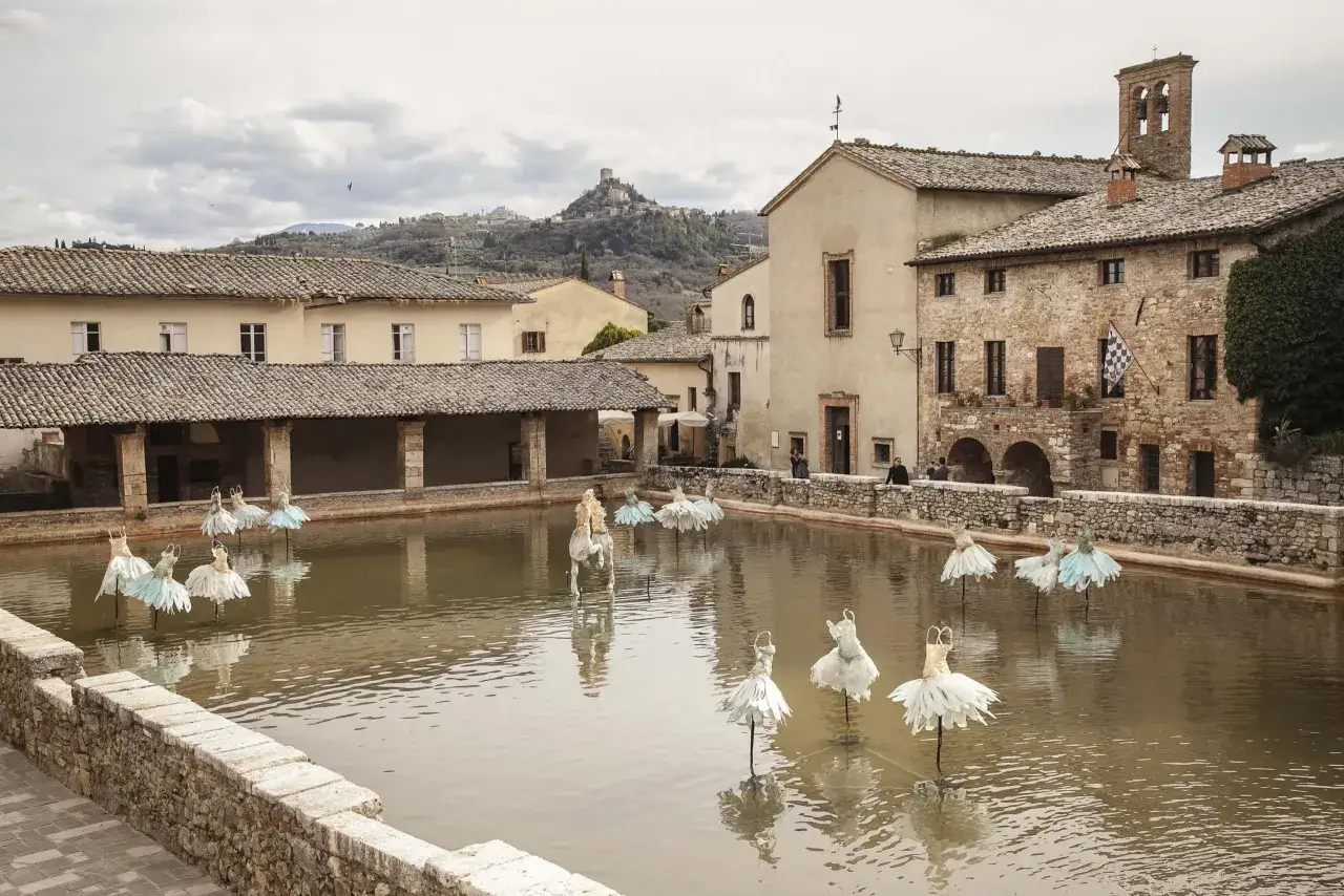 Installazioni di abiti da ballo galleggianti nei Bagni di Vignone, con un castello in lontananza.
