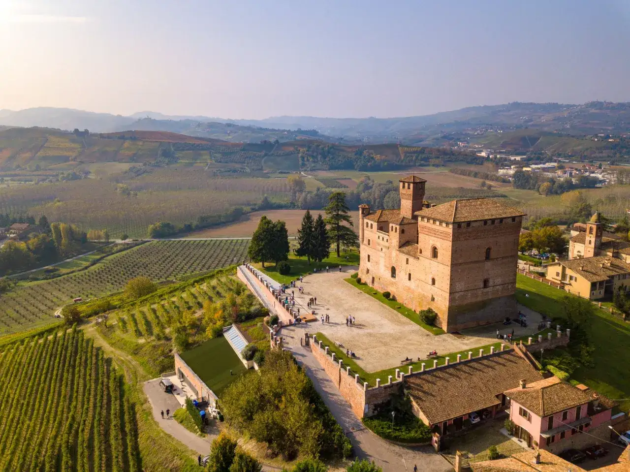 Castello medievale tra i vigneti delle Langhe, con colline ondulate e borghi all'orizzonte.