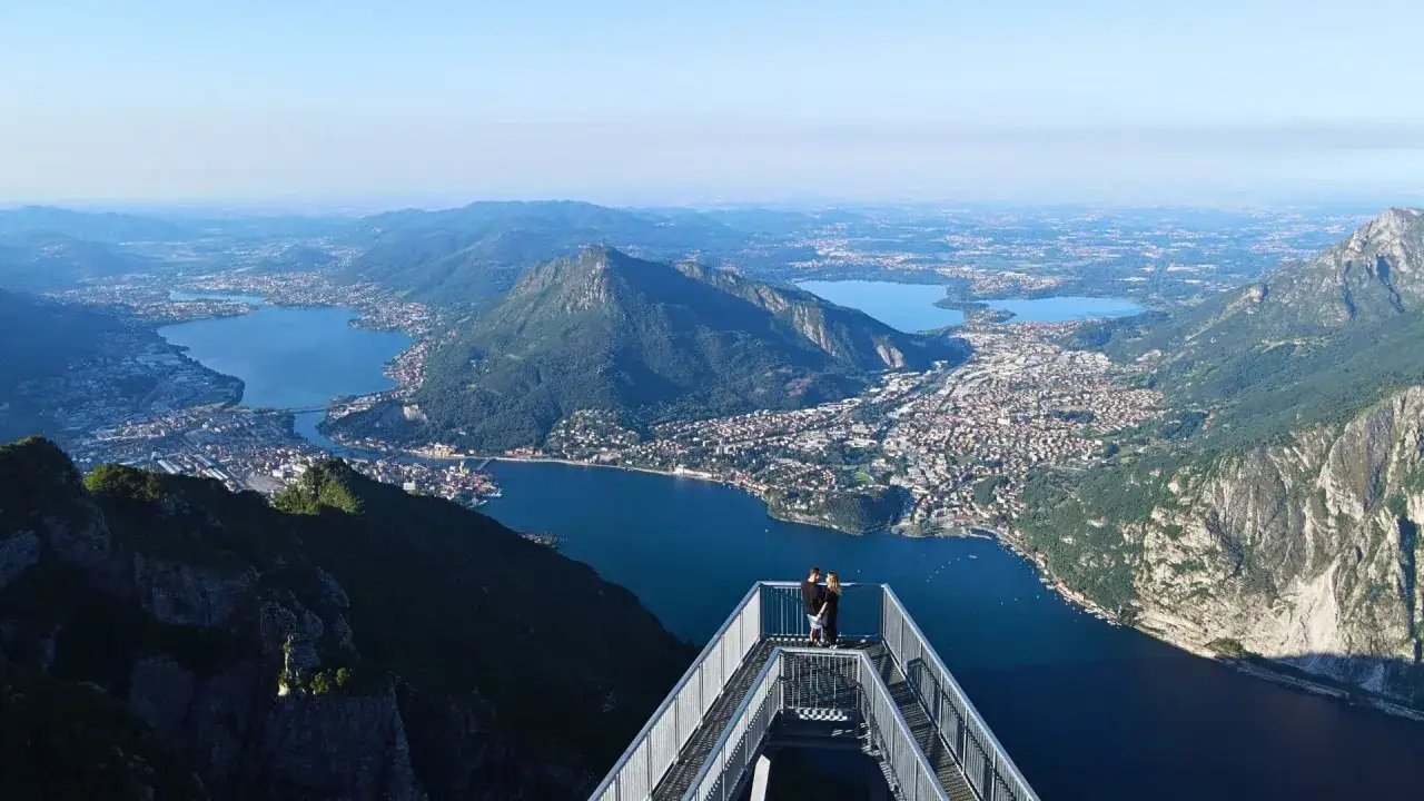 Coppia ammira il panorama mozzafiato dei laghi e delle montagne di Lecco da una passerella panoramica. I sentieri lecchesi offrono viste spettacolari.