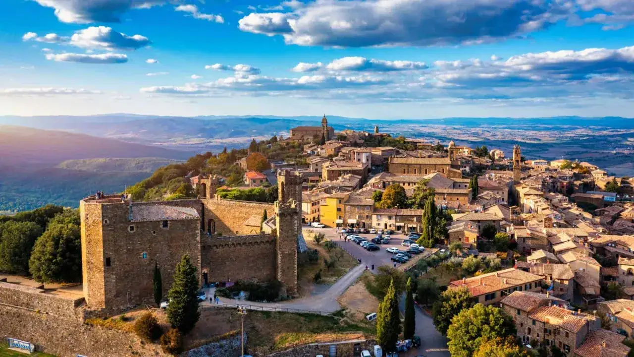 Borghi Bandiera Arancione: un castello medievale domina un pittoresco paese toscano, con tetti in terracotta e colline ondulate all'orizzonte.