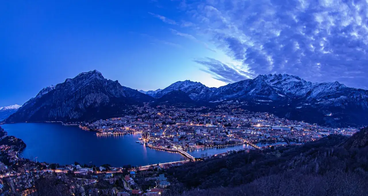 Le luci della città si riflettono sul lago, abbracciate dalle maestose montagne Lecco.