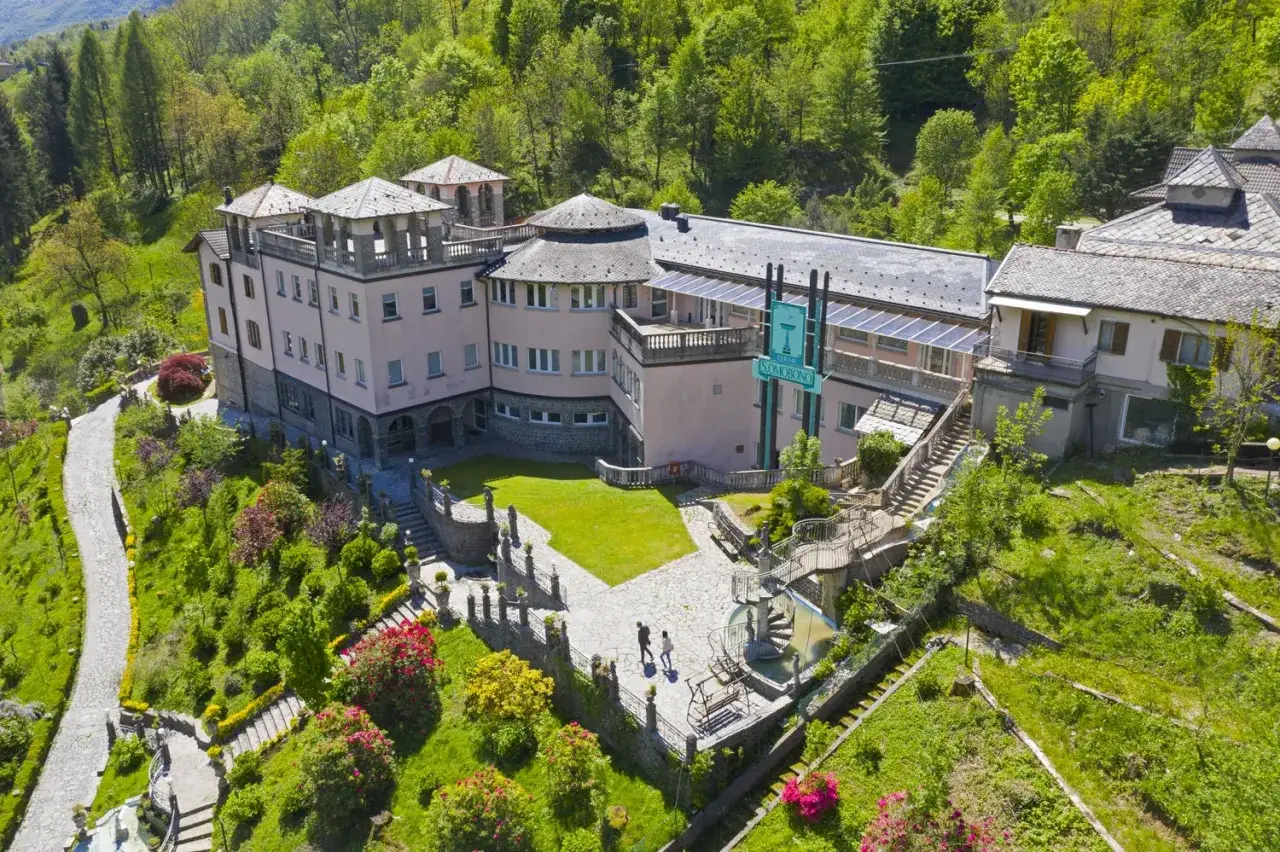 Edificio storico a Sant'Omobono Terme, immerso nel verde, con giardini curati e un sentiero panoramico.