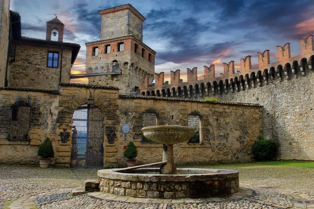 Cortile di un castello medievale, uno dei borghi vicino Parma, con fontana, mura merlate e cielo drammatico.