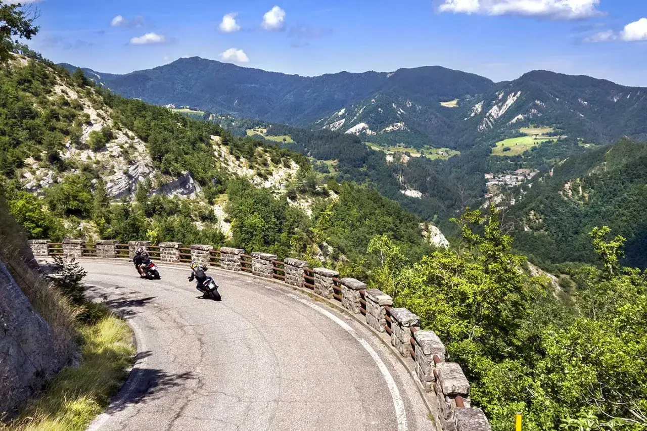 Due motociclisti affrontano una curva panoramica in Emilia Romagna, immersi nel verde delle colline.