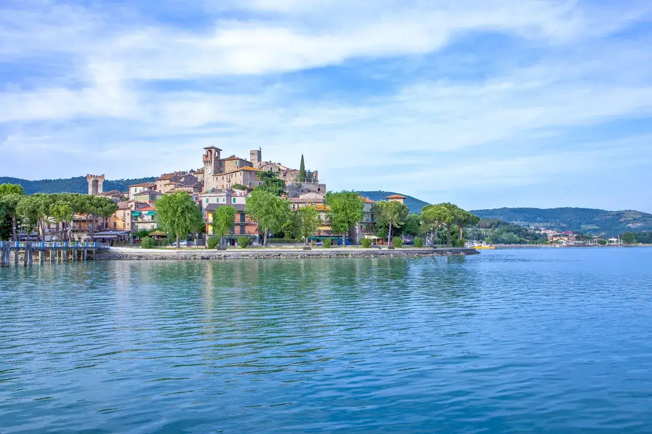 Borgo medievale sul lago, con torri e case colorate. Un luogo incantevole dove si trova Todi, con acque azzurre e colline sullo sfondo.