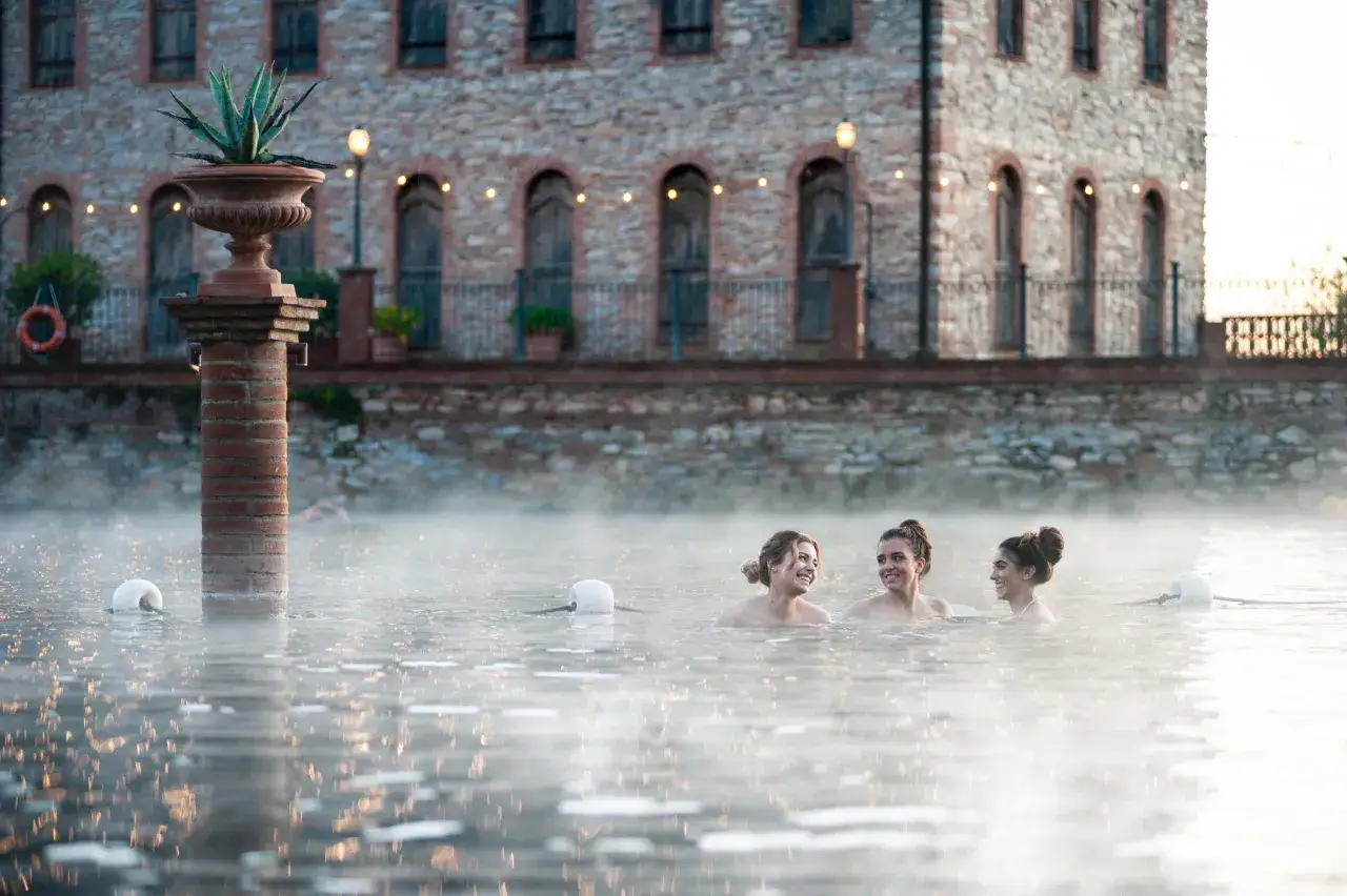 Tre amiche ridono nell'acqua fumante di una piscina termale, un'oasi di relax a Venturina Terme, gratuita e rigenerante.