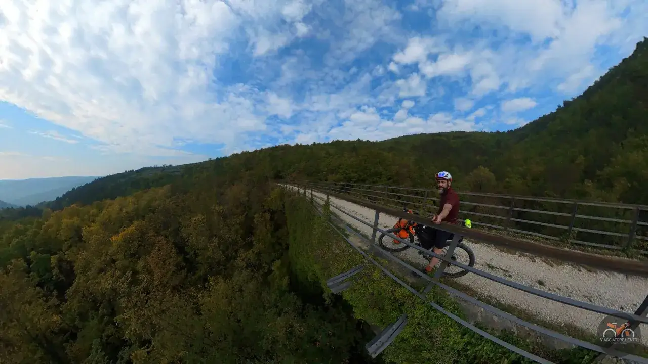 Ciclista con bici da turismo sulla Parenzana, immerso nel verde e sotto un cielo azzurro con nuvole.