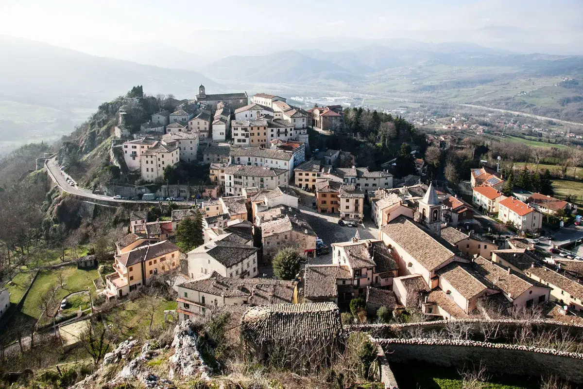 Panoramica aerea di Pennabilli, Rimini, con case in pietra e tetti in tegole rosse arroccate su una collina, circondate da dolci colline.