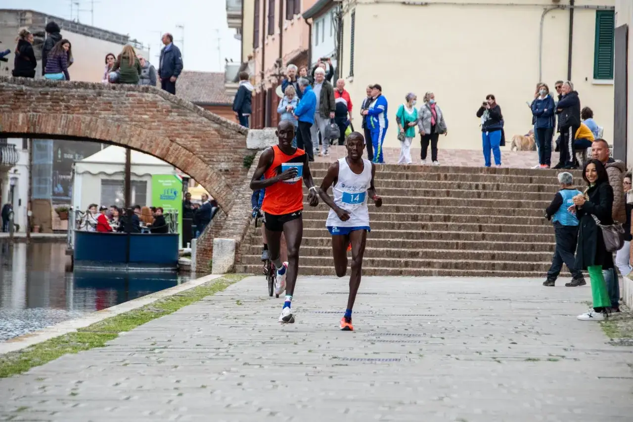 Atleti in gara a Comacchio, un evento di running in Emilia Romagna. Spettatori lungo il canale osservano la competizione.