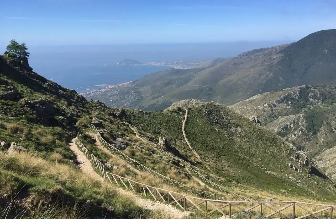 Sentiero panoramico tra le montagne del Lazio, con vista sul mare e una cittadina costiera.