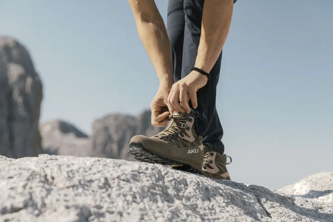 Mani che allacciano scarpe da hiking AKU su rocce. Il loro significato è avventura e sicurezza in montagna.