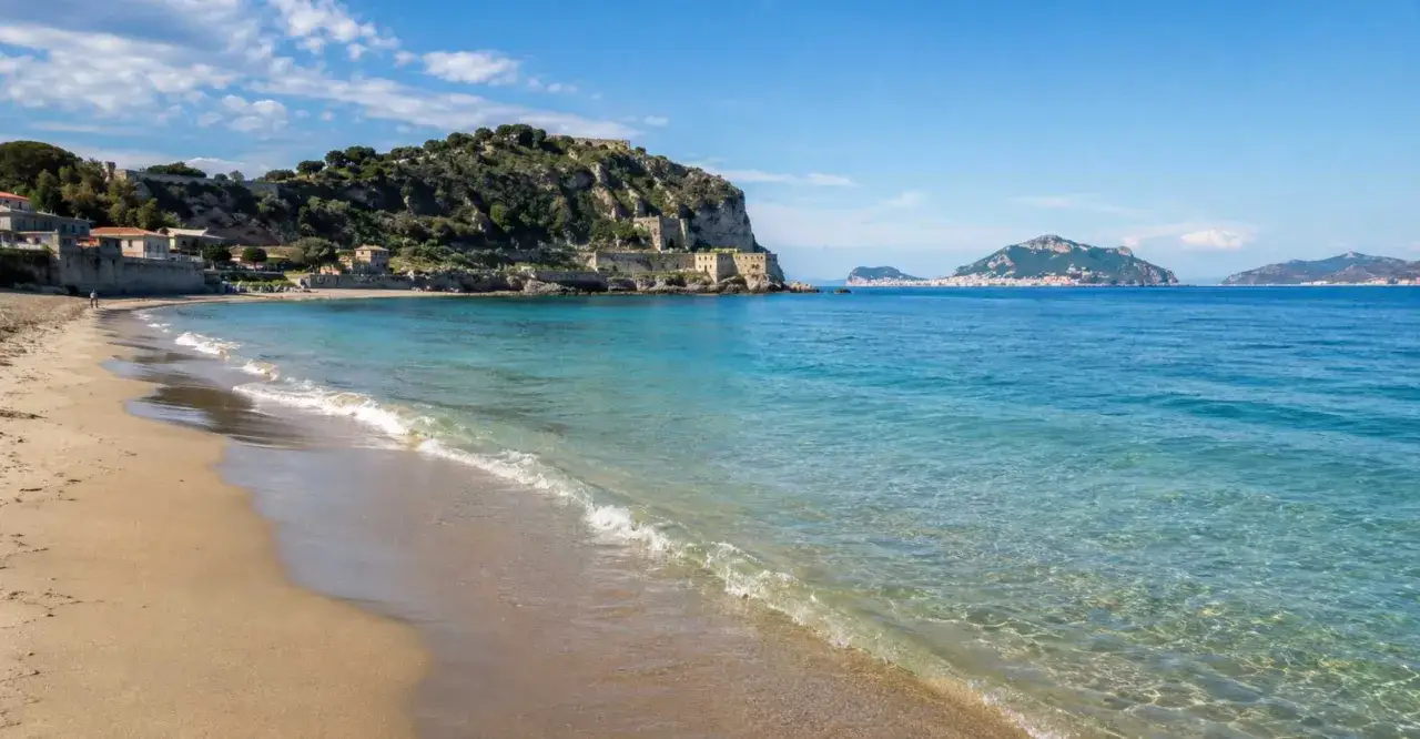 Spiaggia dorata baciata da acque cristalline, con un antico borgo arroccato sulla collina. Un incantevole mare vicino Napoli, con isole all'orizzonte.
