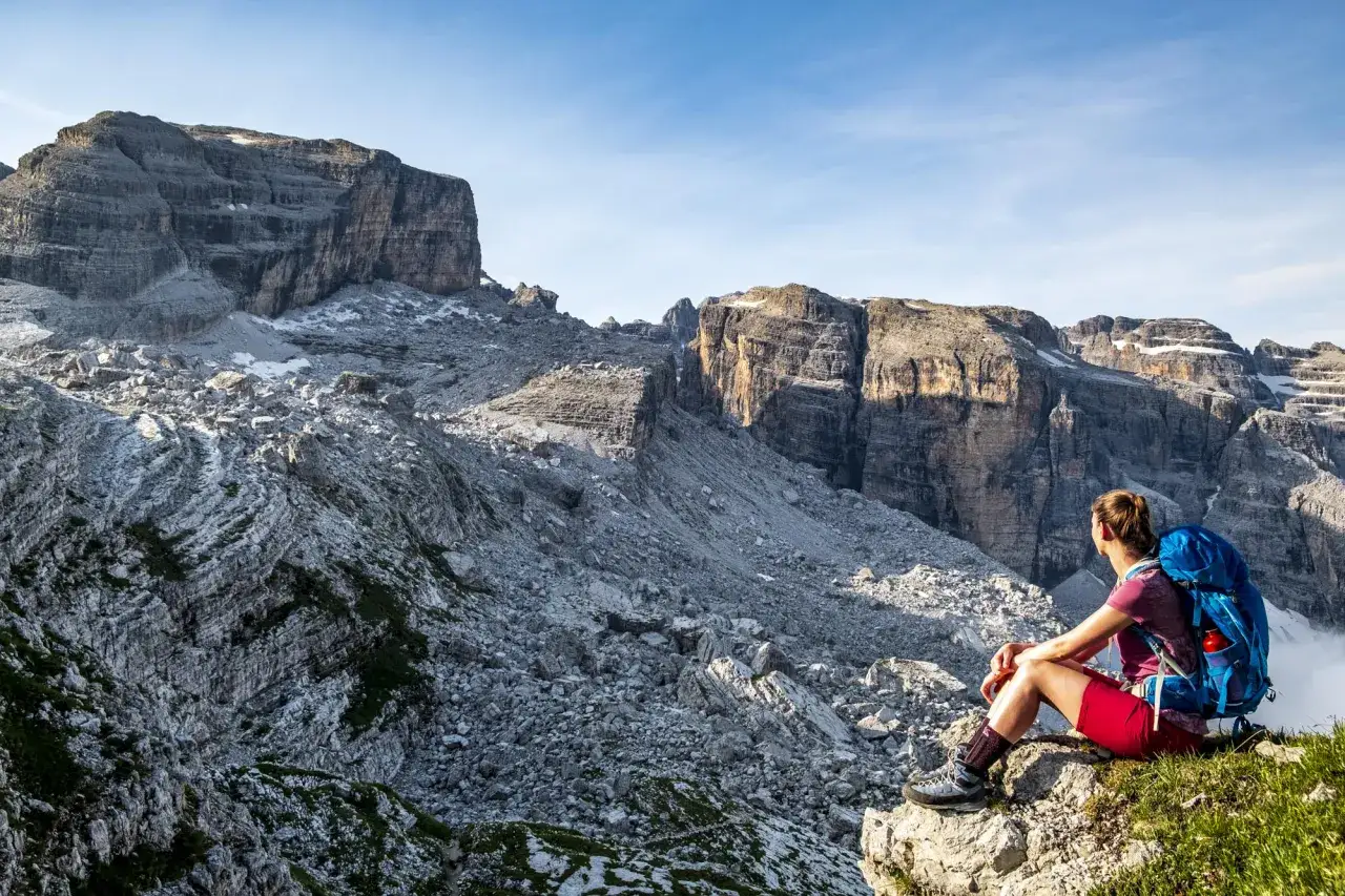 Donna con zaino blu ammira il panorama roccioso, perfetta per escursioni ad Andalo.