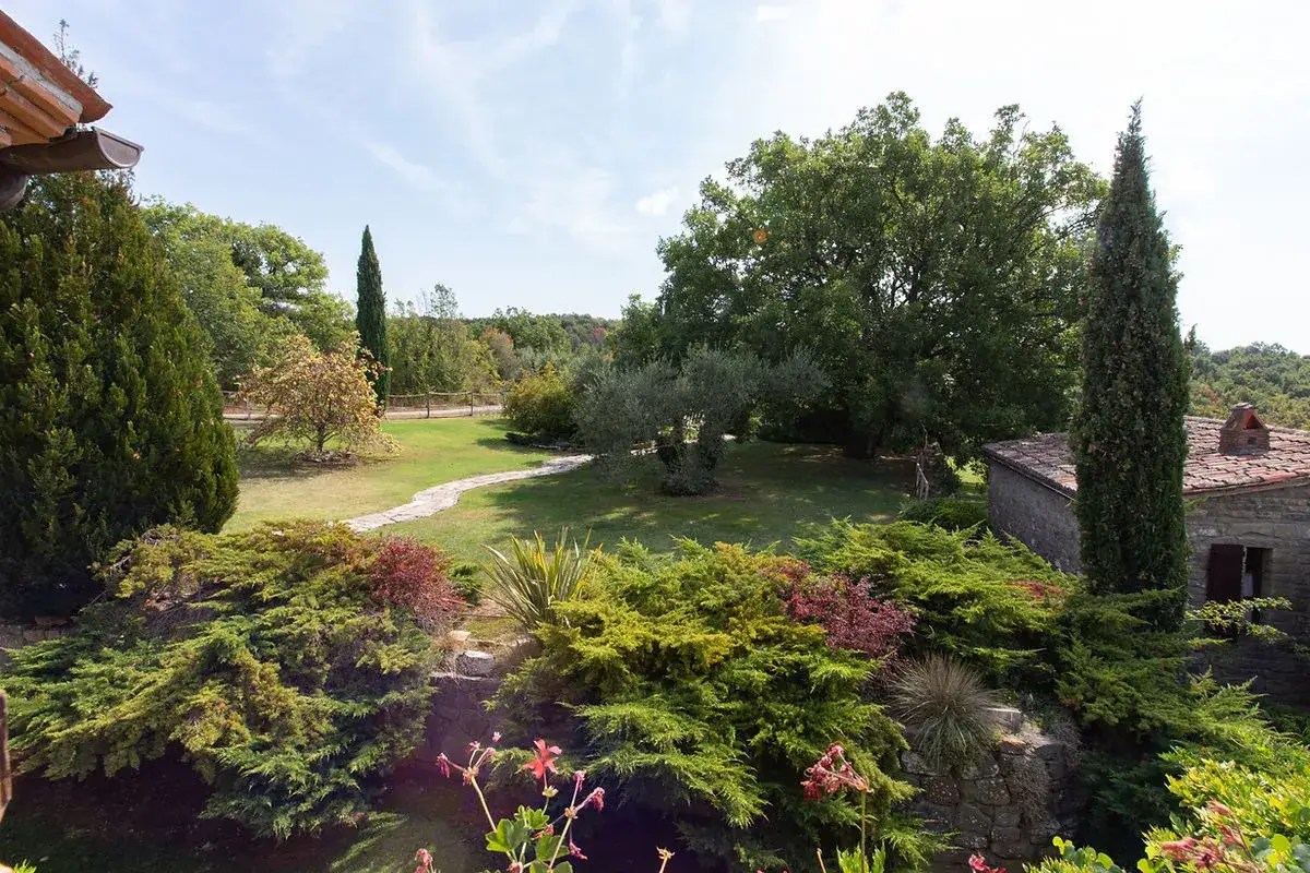 Un giardino lussureggiante con un sentiero in pietra, alberi secolari e un casolare in pietra. Un luogo incantevole dove scoprire cosa vedere a Parrano.