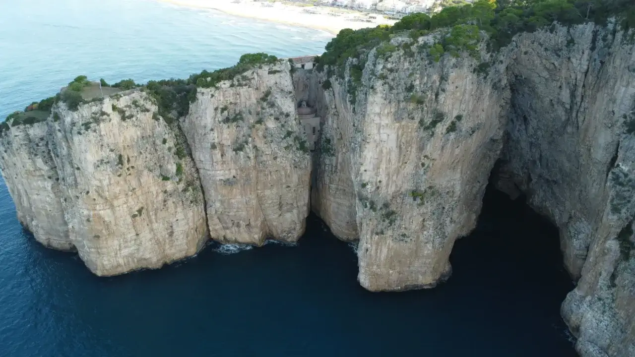 La leggenda della Montagna Spaccata a Gaeta: imponenti falesie calcaree si ergono sul mare blu, con una fenditura che nasconde un santuario.