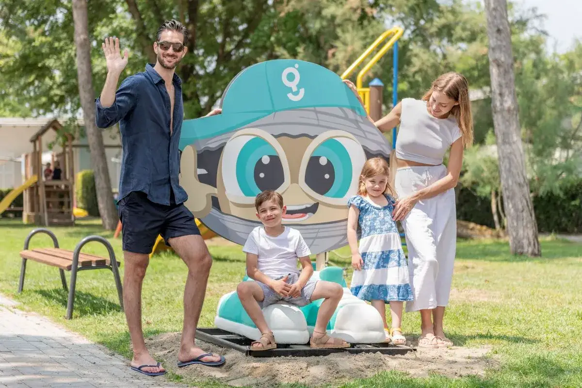 Famiglia felice a Comacchio con bambini, sorridono accanto a un simpatico personaggio animato in un parco giochi.