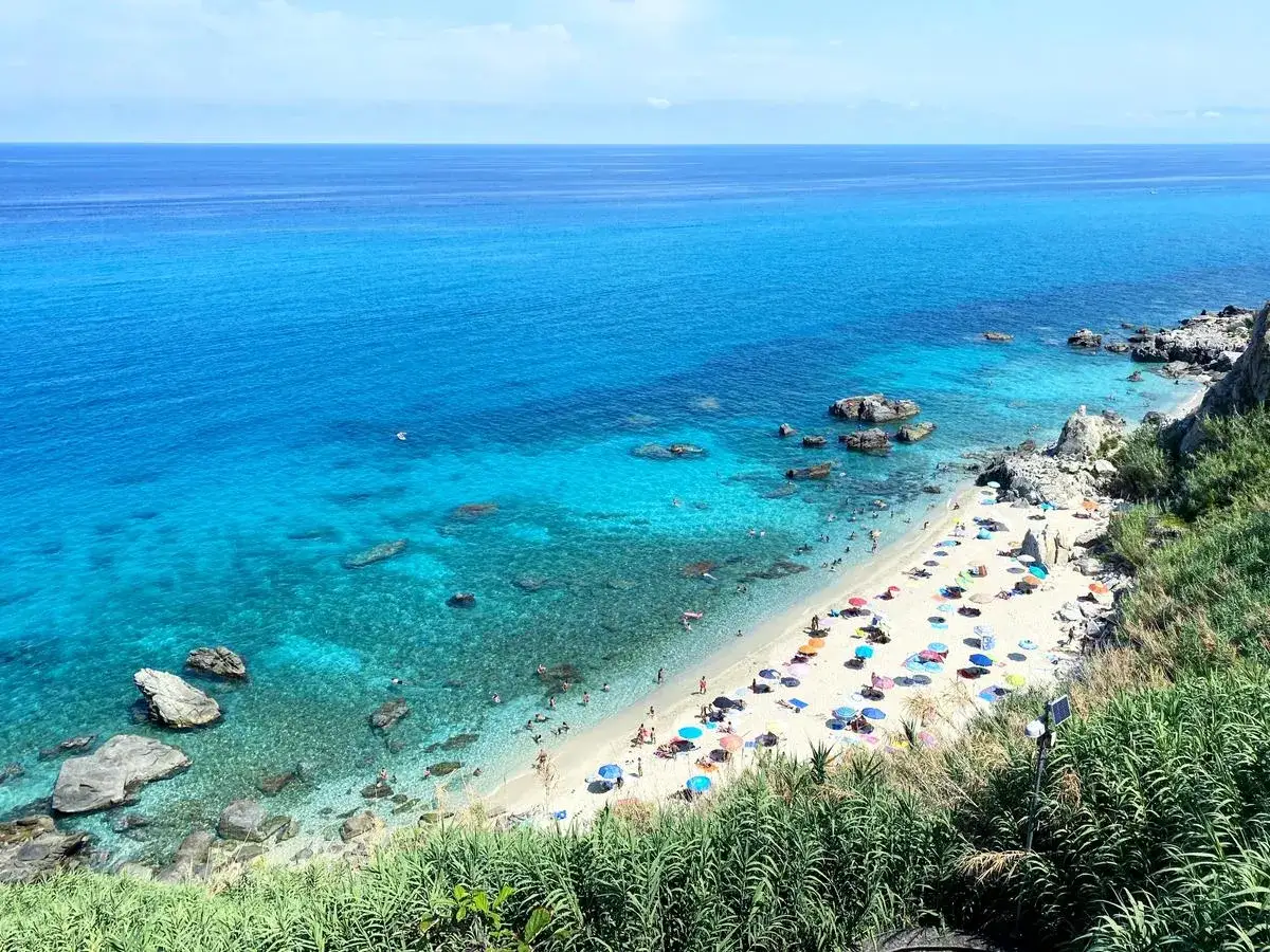 Spiaggia bianca affollata di ombrelloni colorati e bagnanti, bagnata da un mare cristallino. Un vero paradiso tra le migliori spiagge Calabria.