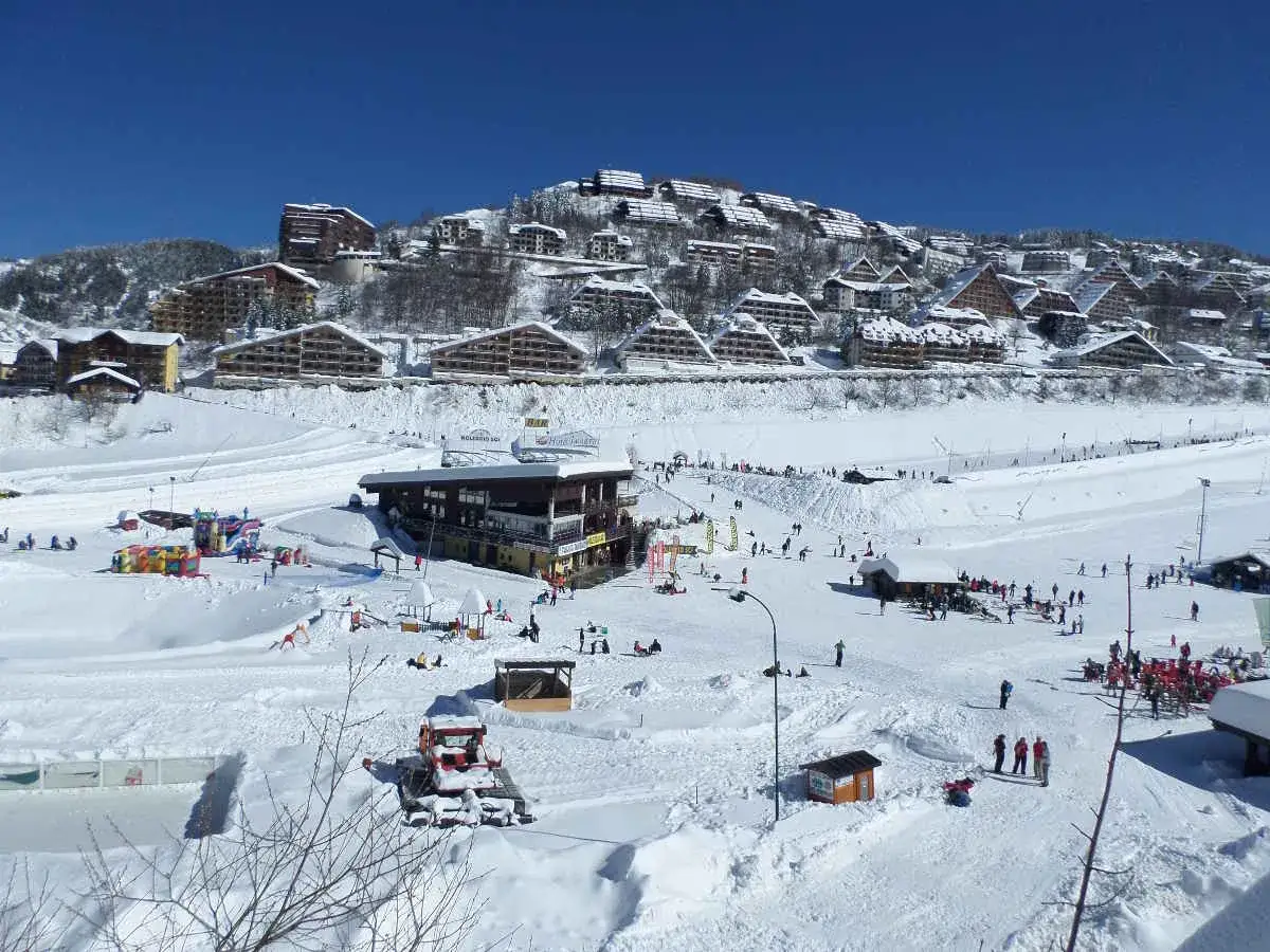 Un paesaggio innevato con edifici in stile alpino, perfetto per una settimana bianca in Piemonte. Piste da sci, rifugi e divertimento per tutti.