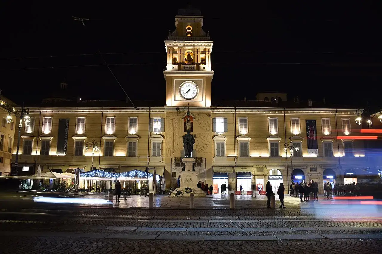 Palazzo del Governatore illuminato di notte, con orologio e statua. Un'ottima idea per cosa vedere a Parma gratis, passeggiando in piazza.