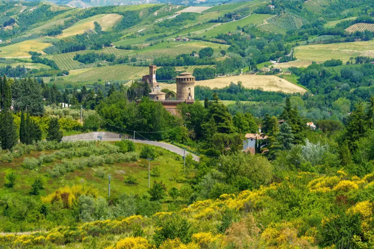 Colline verdi e campi coltivati in Emilia Romagna, con un castello in lontananza. Un invito a percorrere le strade panoramiche.