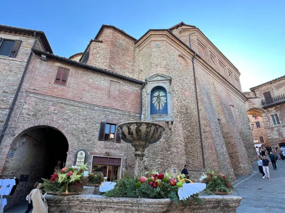 Fontana decorata nel borgo Panicale, Umbria. Edifici in pietra e mattoni, cielo azzurro.