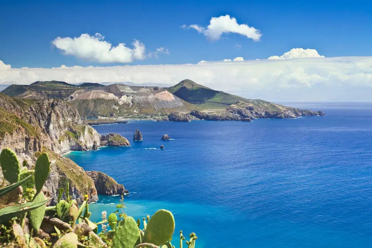 Scogliere rocciose e vegetazione lussureggiante si affacciano sul blu intenso del mare Lipari, con isole vulcaniche sullo sfondo.