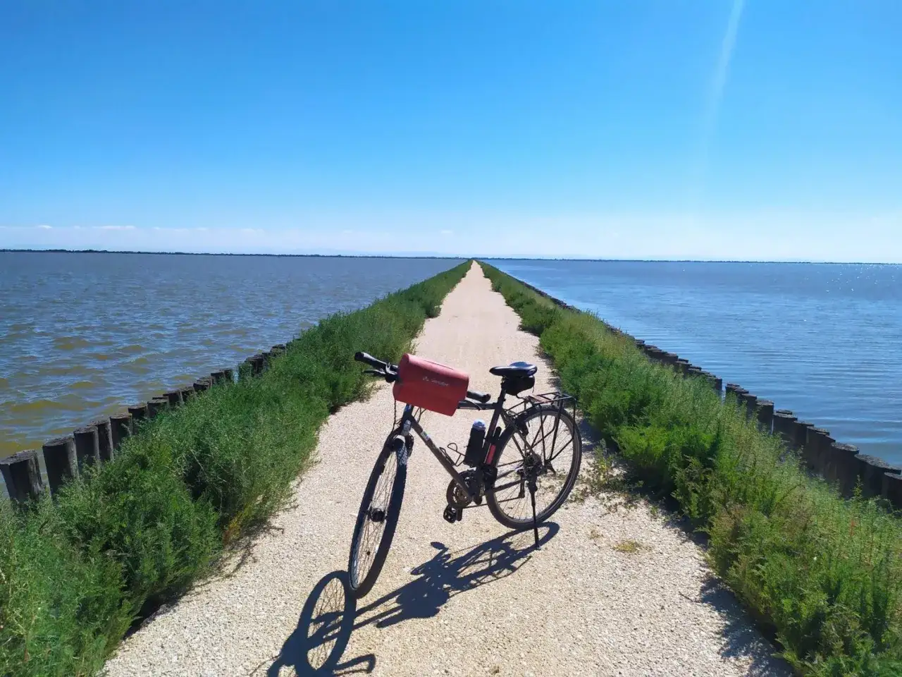 Bicicletta ferma su una pista ciclabile che si estende all'infinito tra acqua e cielo azzurro, un invito a esplorare il Lido di Spina.