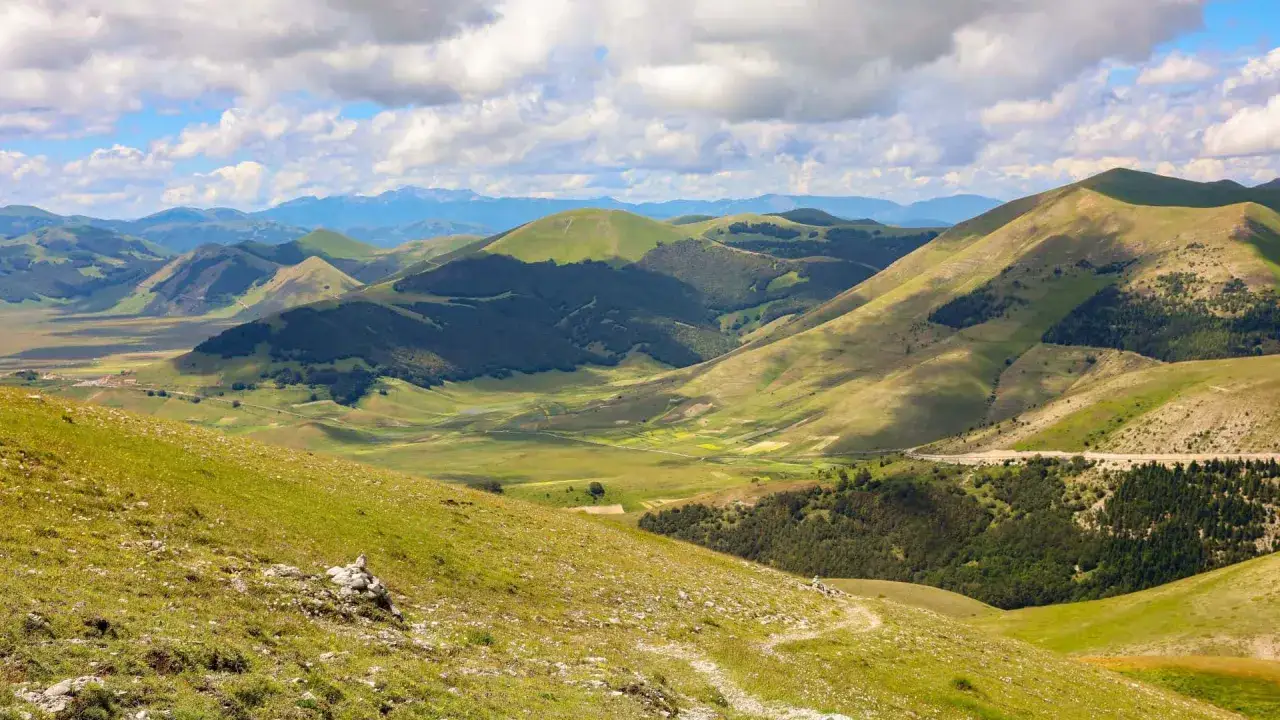 Panoramica dei Monti Sibillini: cosa vedere in questo paesaggio verdeggiante con dolci colline, boschi e un cielo nuvoloso.