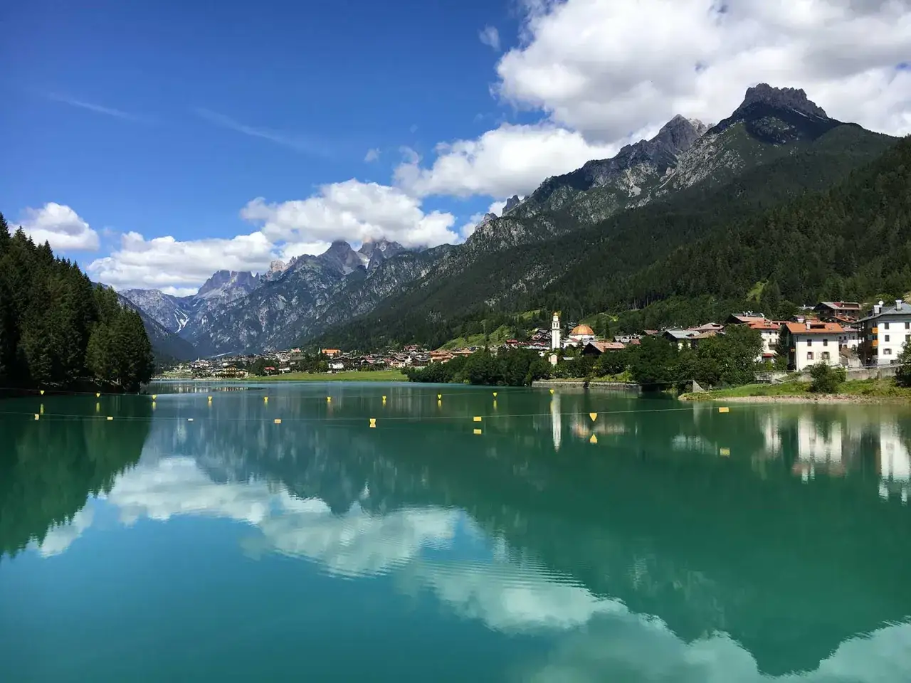 Lago turchese con riflessi montani e un villaggio alpino. Perfetto per passeggiate facili in Cadore.