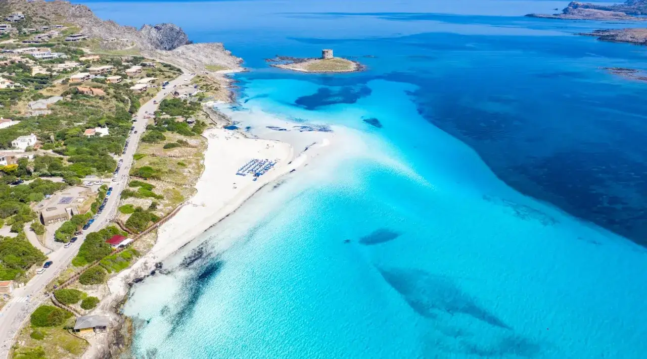 Spiaggia di sabbia bianca baciata da acque turchesi cristalline, con una torre antica in lontananza.
