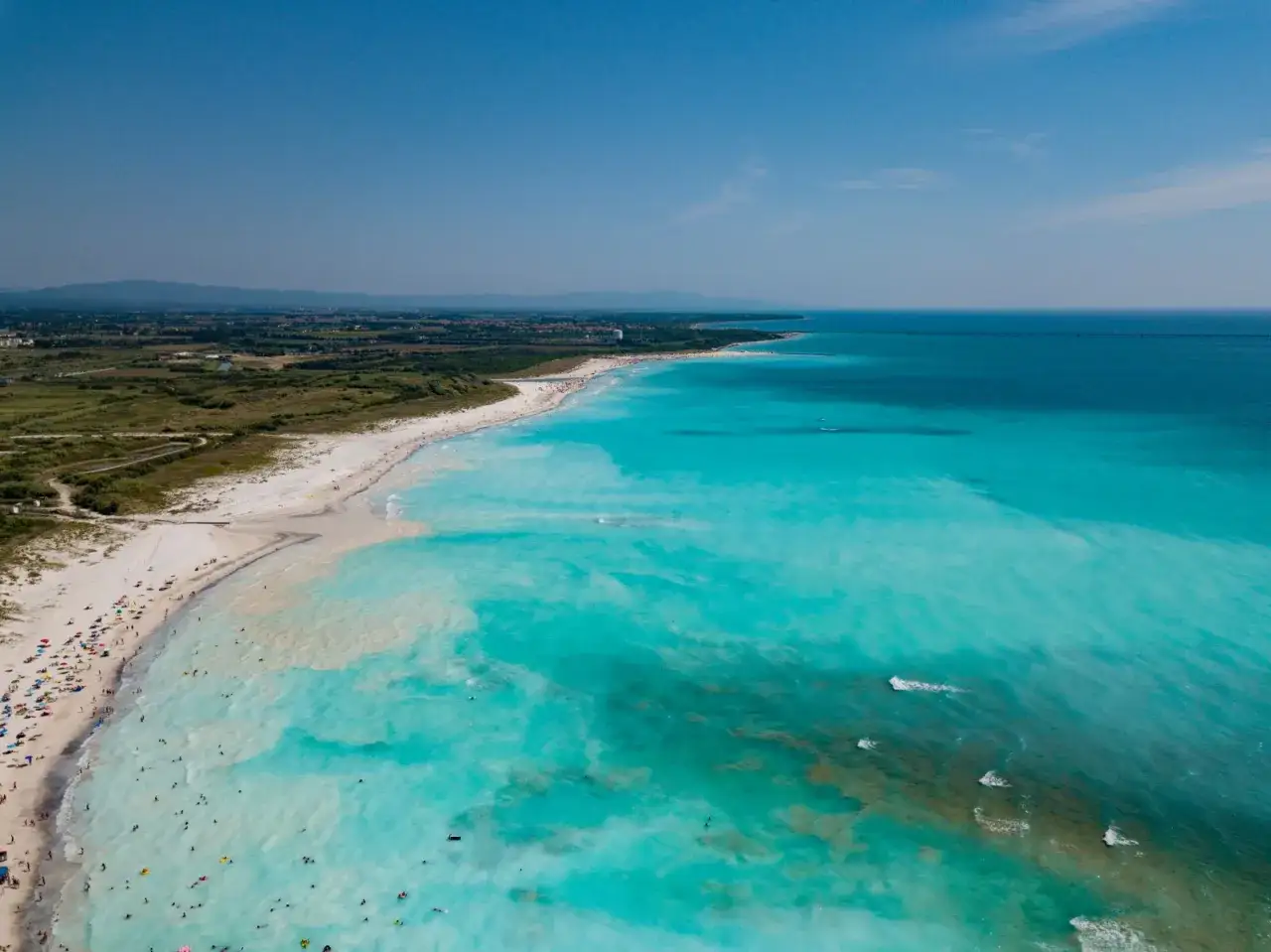 Vasta distesa di spiagge bianche bagnate da un mare turchese cristallino, con bagnanti che si godono il sole e l'acqua.