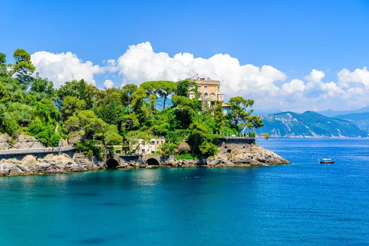Villa sul mare a Santa Margherita Ligure, con un castello in cima alla collina, circondata da vegetazione lussureggiante e affacciata sul blu intenso del mare.
