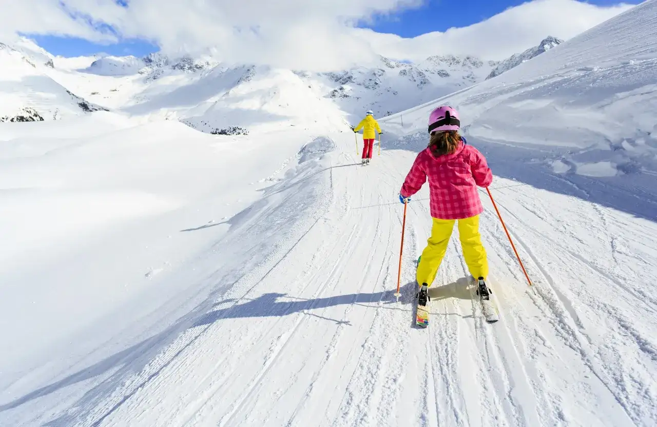 Bambini imparano a sciare su piste da sci per principianti, con montagne innevate sullo sfondo.