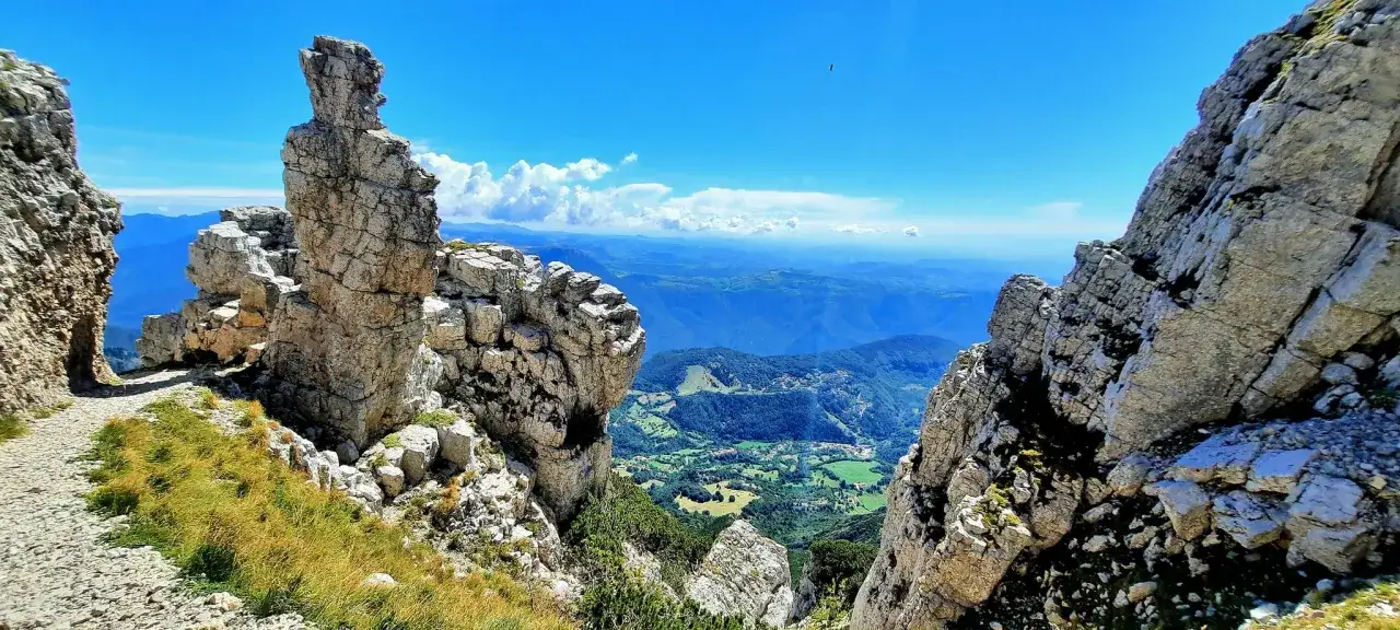 Sentiero roccioso sul Monte Baldo, cosa vedere: panorami mozzafiato su valli verdi e montagne azzurre sotto un cielo limpido.
