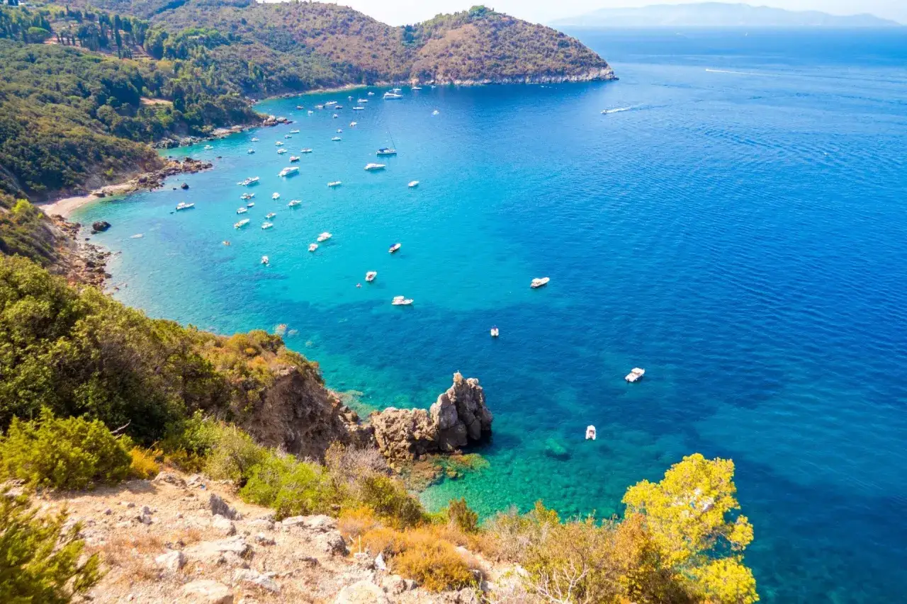 Baia incantevole nel mare della Maremma Toscana, con acque cristalline e numerose barche che solcano il blu intenso.