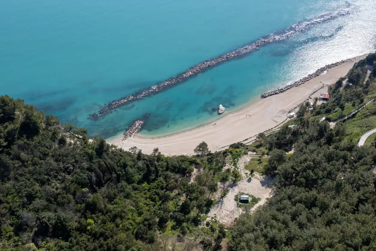 Vista aerea di una spiaggia dorata e mare turchese, una località mare Marche incantevole con scogliere e vegetazione rigogliosa.