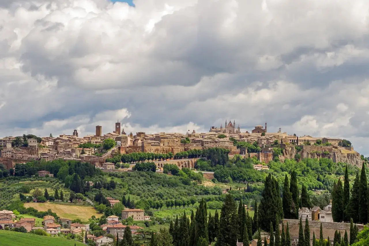 Panoramica di una città dell'Umbria arroccata su una collina, con edifici storici, un duomo imponente e vegetazione lussureggiante.