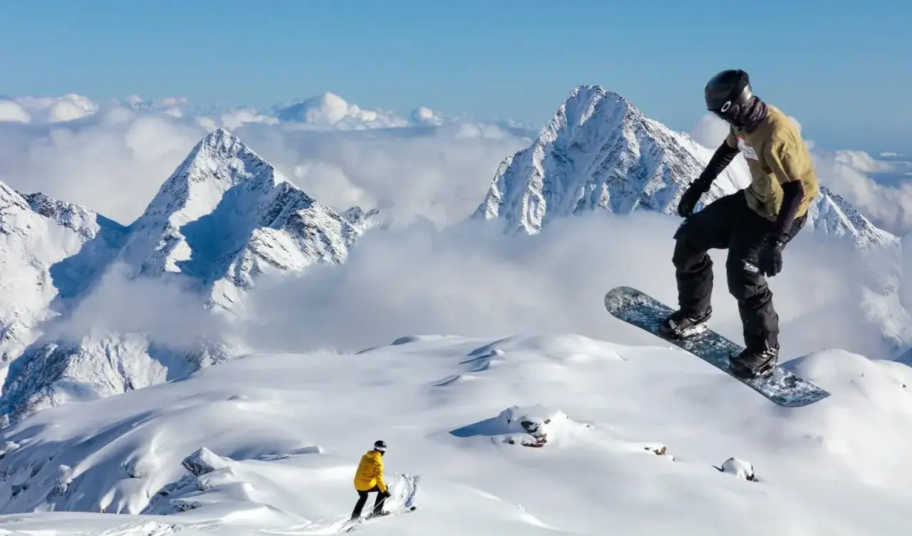 Snowboarder in volo su montagne innevate, uno sciatore più in basso. Posti belli in montagna Piemonte inverno, un sogno bianco.