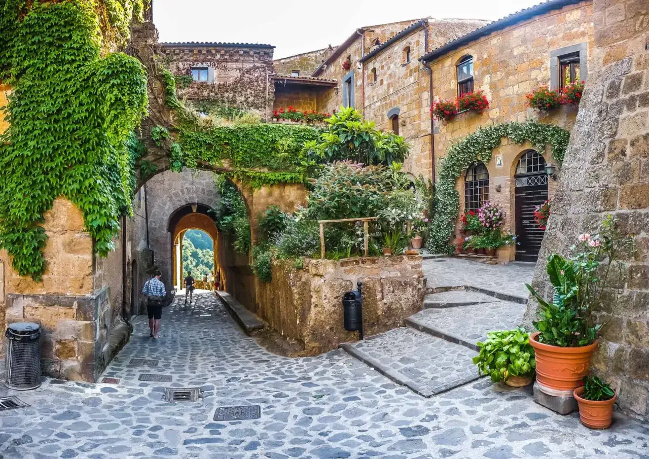 Un vicolo acciottolato tra antiche case in pietra, ricoperte di edera e fiori, evoca la magia de i 5 borghi più belli delle Marche.