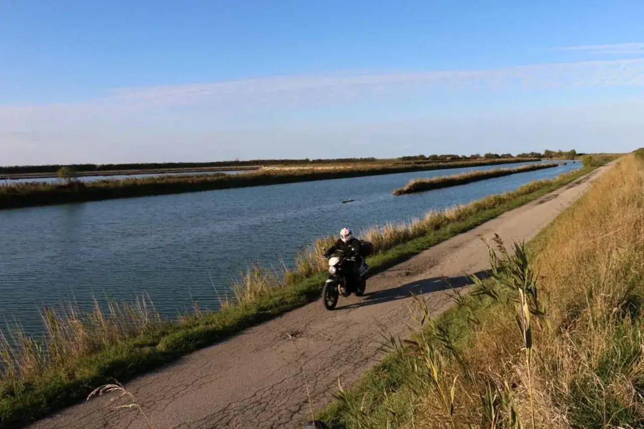 Un motociclista esplora il Delta del Po, godendosi il paesaggio di canali e vegetazione rigogliosa sotto un cielo azzurro.