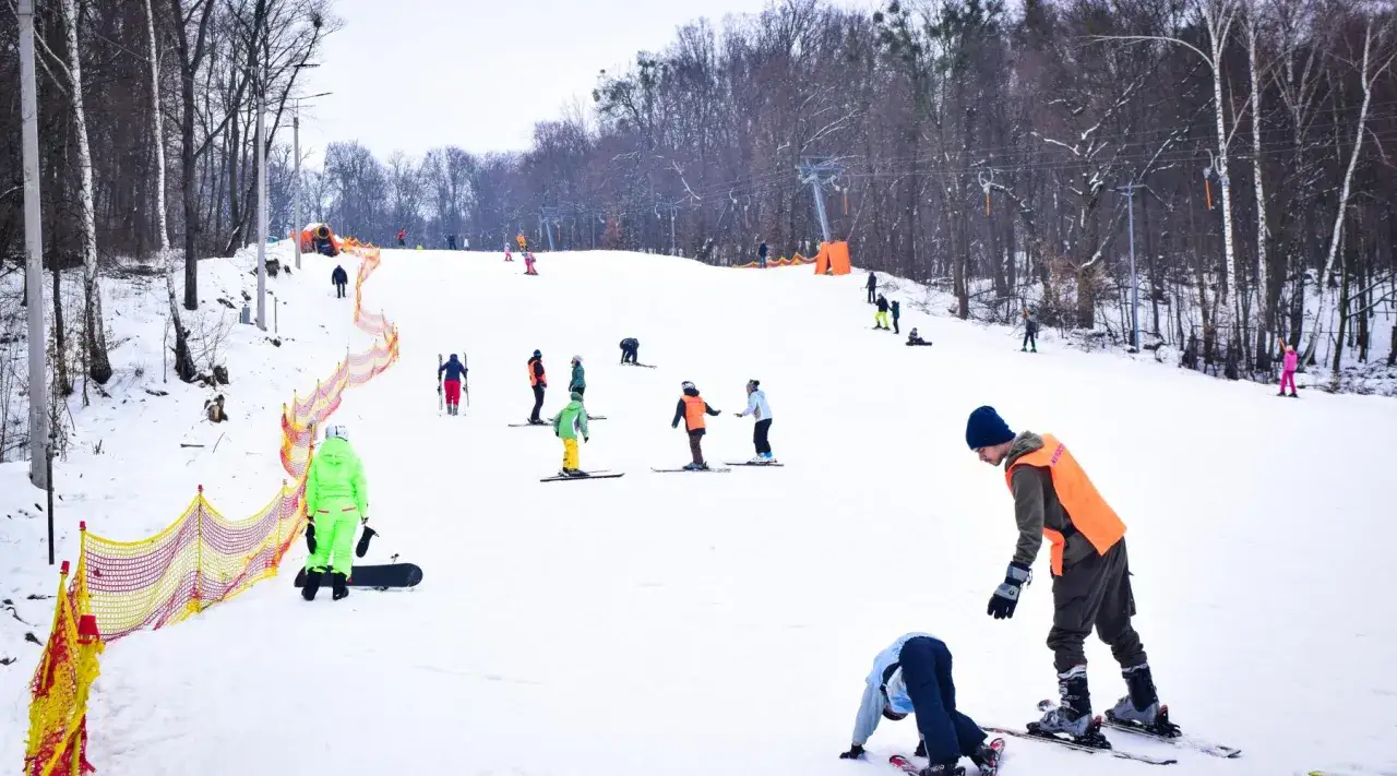 Bambini e adulti sciano e fanno snowboard sui impianti sciistici del centro Italia. Un istruttore con pettorina arancione guida gli allievi.