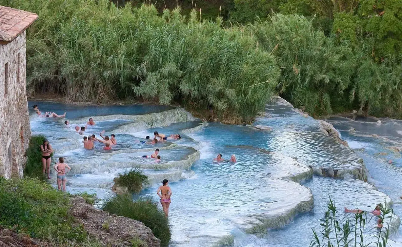 Persone si rilassano nelle cascate naturali delle terme sud Italia, circondate da vegetazione lussureggiante.