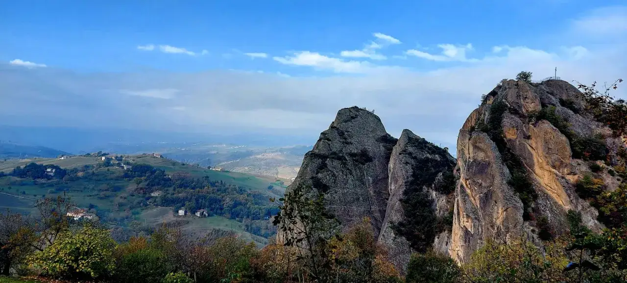 Vette rocciose del monte battaglia si stagliano su un paesaggio collinare con case sparse e alberi autunnali.