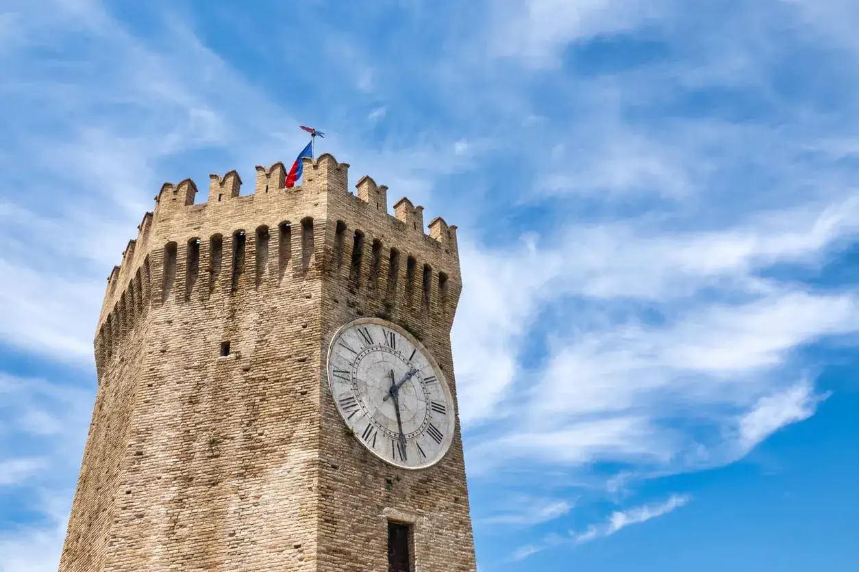 Torre dell'orologio a Gualtieri, con bandiera tricolore e cielo azzurro.