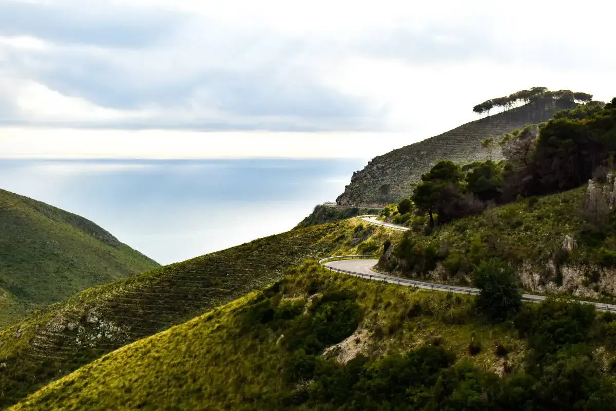Strada tortuosa lungo la costa, ideale per un via francigena in bici percorso panoramico. Mare azzurro e colline verdi.