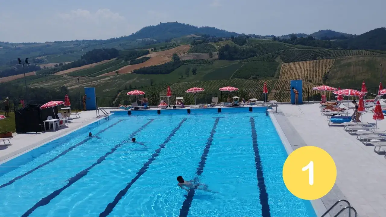 Piscina con persone che nuotano e si rilassano, con vista su colline coltivate. Ideale per scoprire le terme Pavia prezzi.