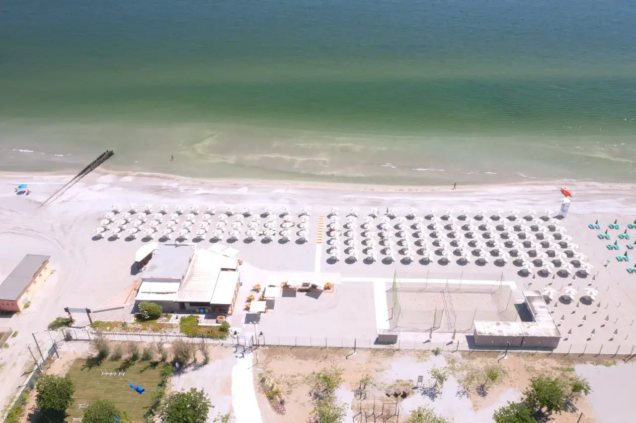 Filetto di spiaggia ordinato con ombrelloni bianchi, una persona in acqua e un campo da beach volley. Tra le spiagge più belle dell'Emilia Romagna.